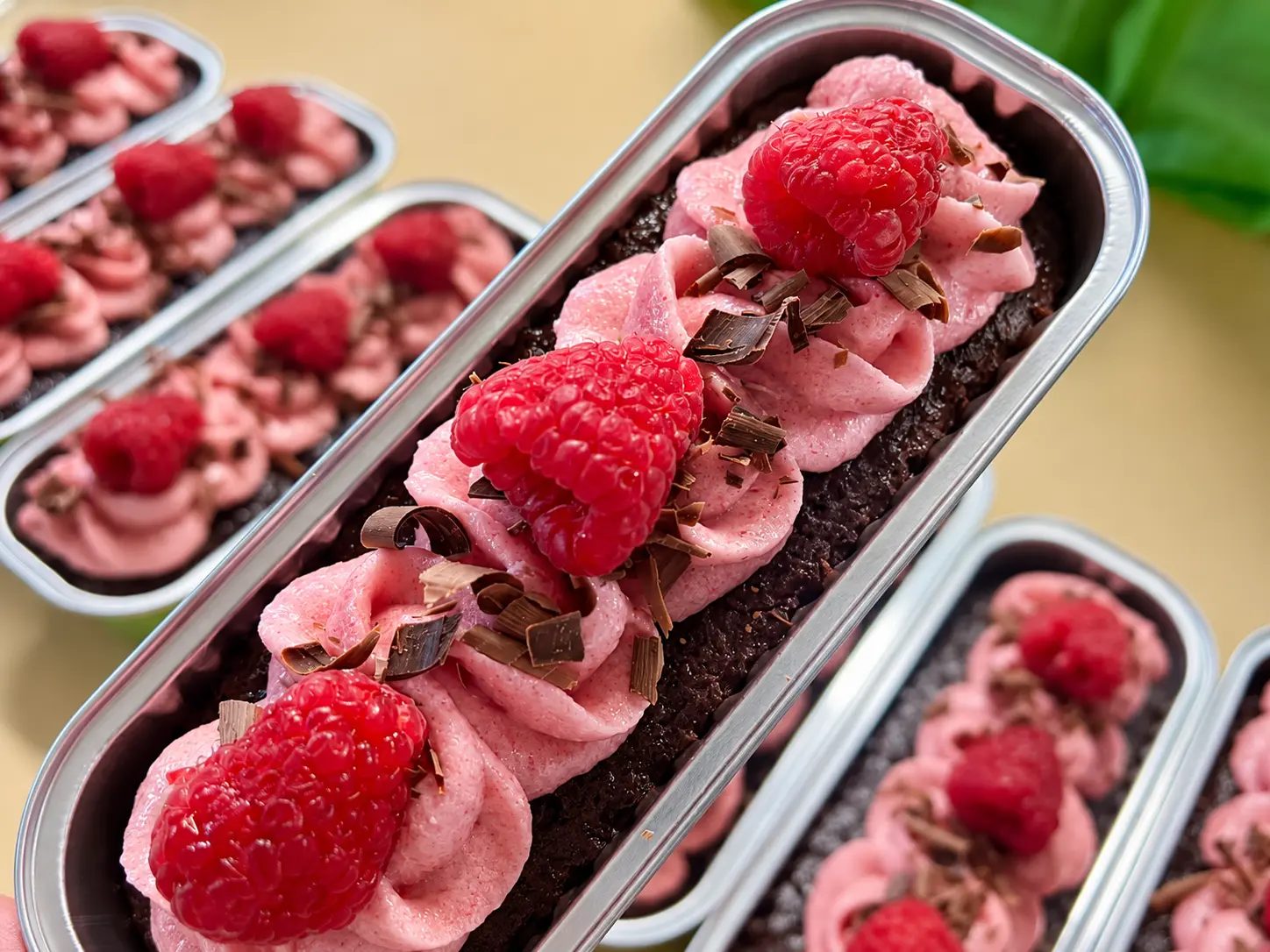 Mini chocolate cakes piped with pink berry buttercream rosettes and topped with chocolate shavings and fresh raspberries