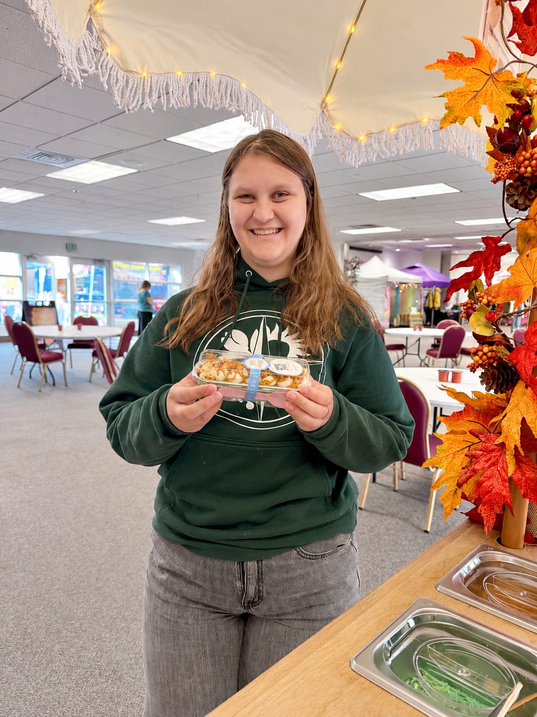 A smiling young guest holding a packaged Sweetly Built mini cake in a clear box tied with ribbon